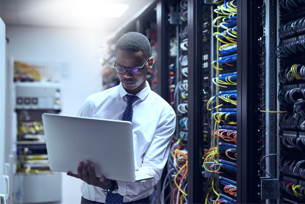 A man working intently on his laptop while surrounded by stacks of computers. 