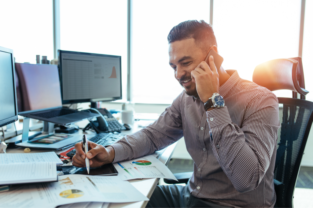 A financial officer smiling on the phone while looking at charts. 