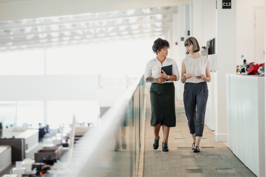 Two women speaking while walking through an office building. 