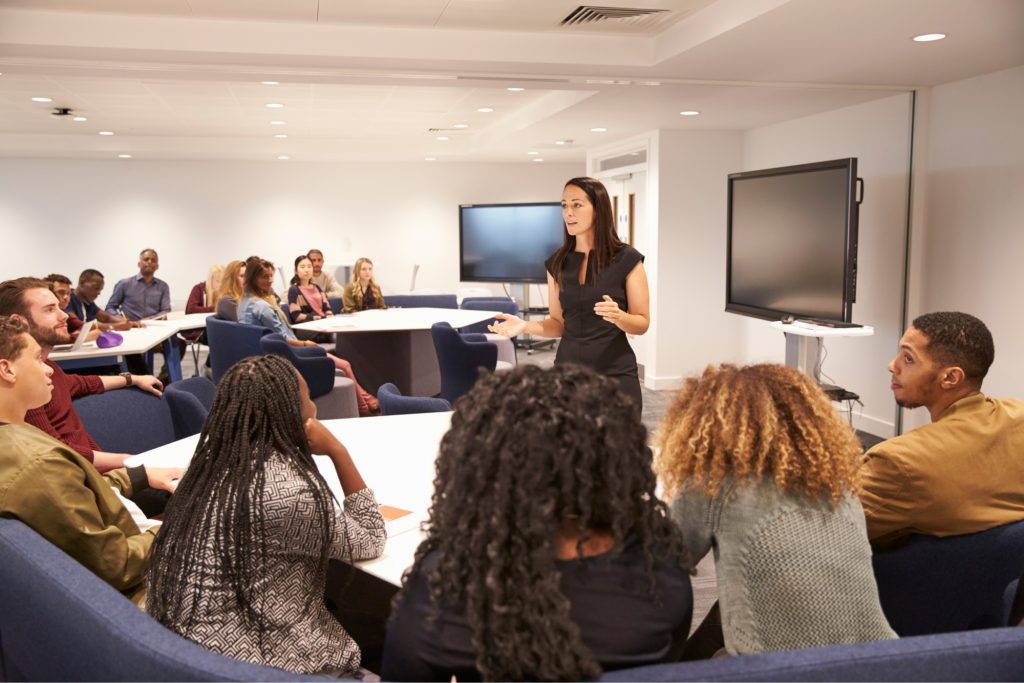 Inside of a college classroom where a professor lectures her students. 