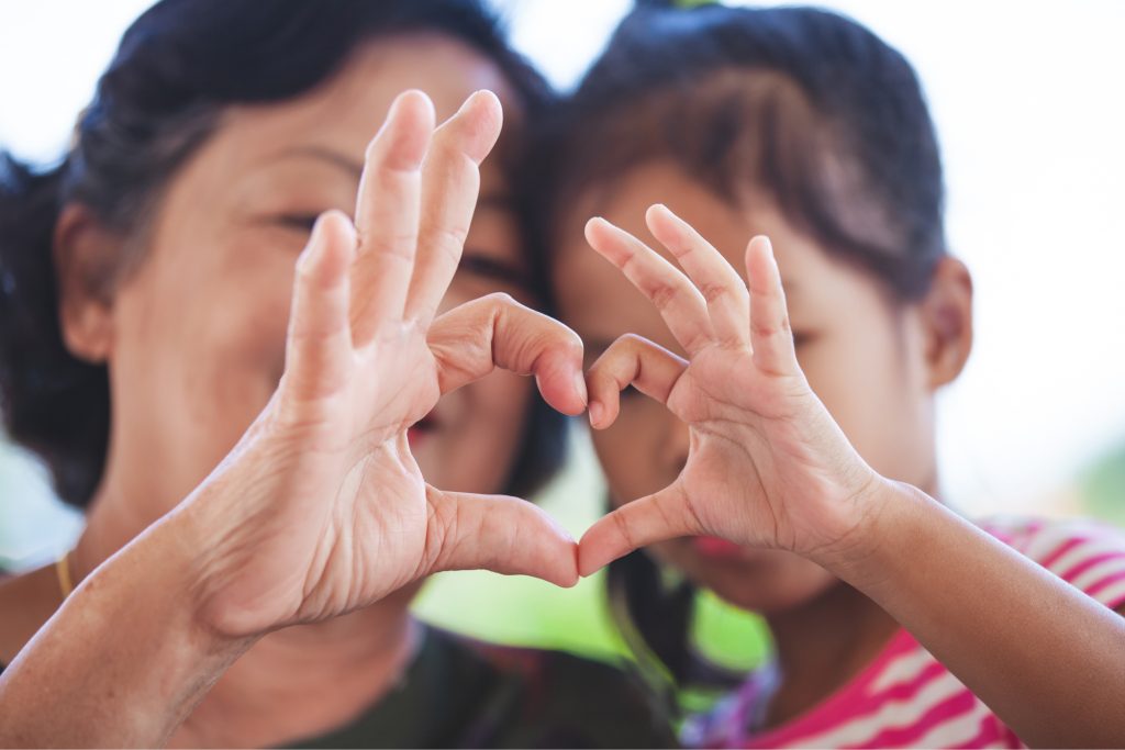 A woman and child holding their hands together to make a heart. 