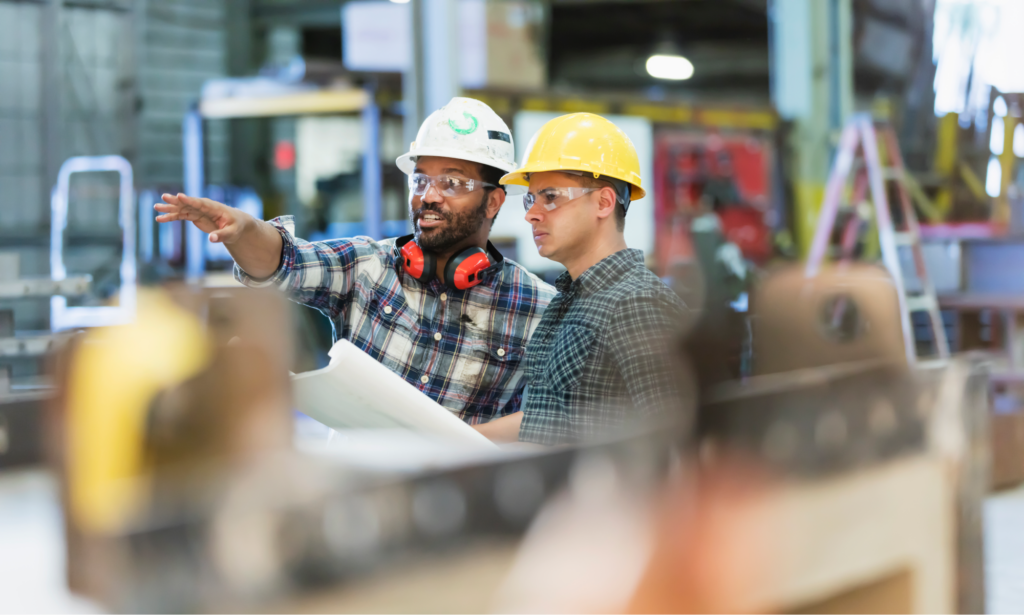 A construction worker teaching another about a facility.  