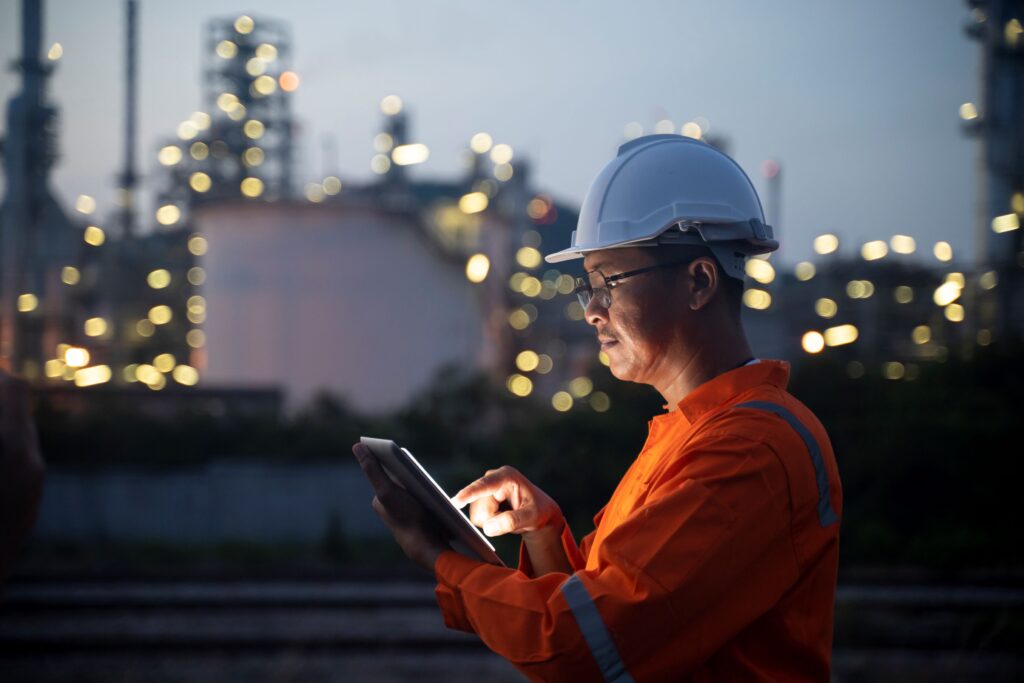 A construction worker outside of a power plant working on his iPad.