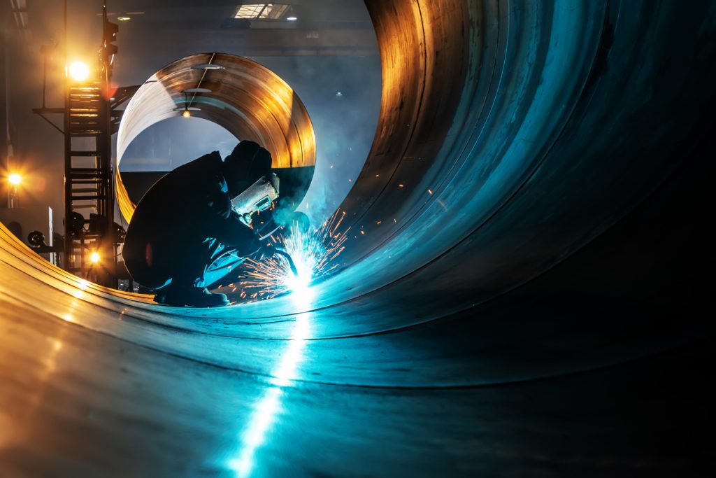 A man welding inside of a large metal cylinder. 