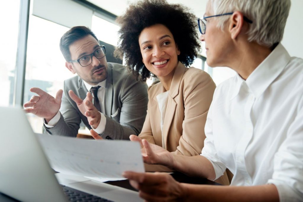 A woman smiling in between two board members discussing charts. 