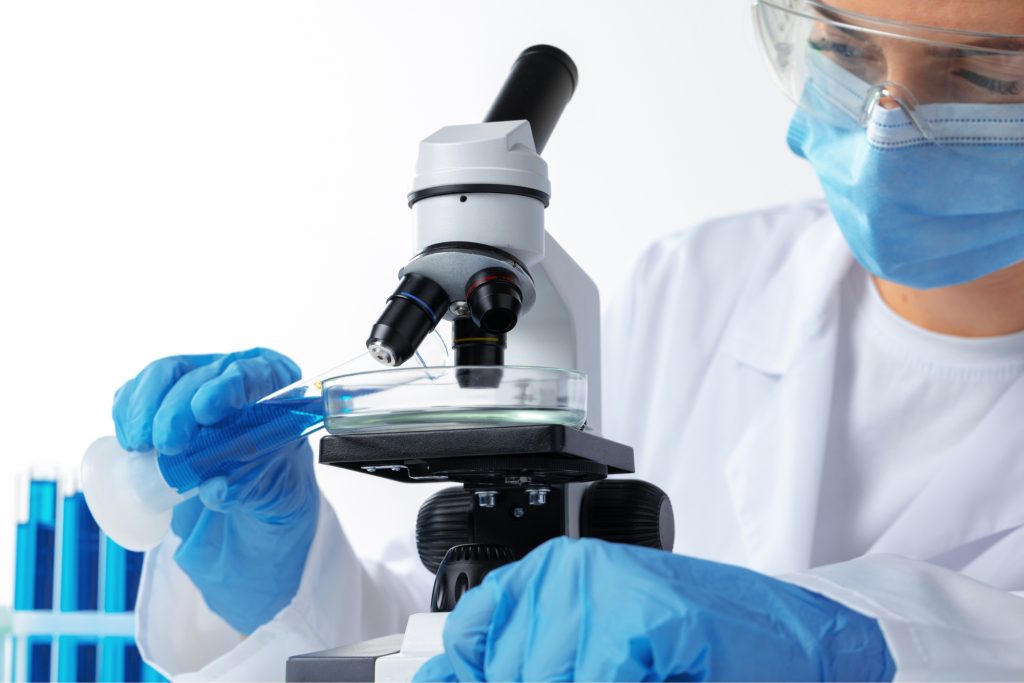 A scientist looking through a microscope at a Petri dish. 