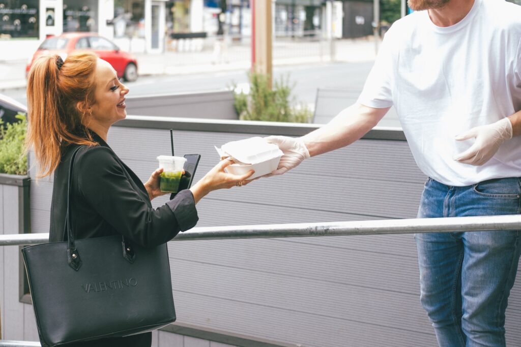 A man handing off a to-go box to a woman outside a restaurant. 